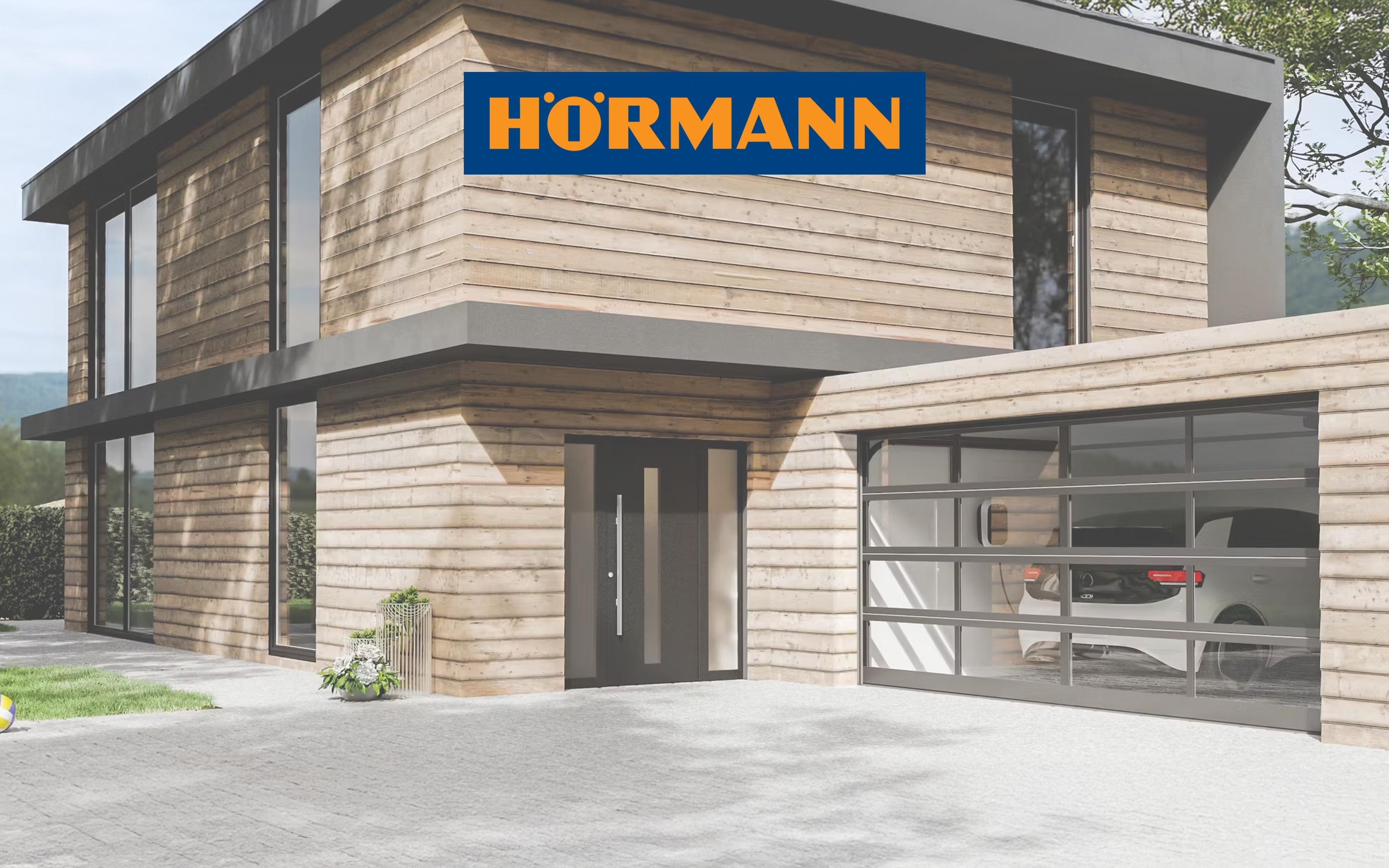 Modernes Holzhaus mit großen Glasflächen und angrenzender Garage mit Sektionaltor, im Vordergrund das Hörmann-Logo.